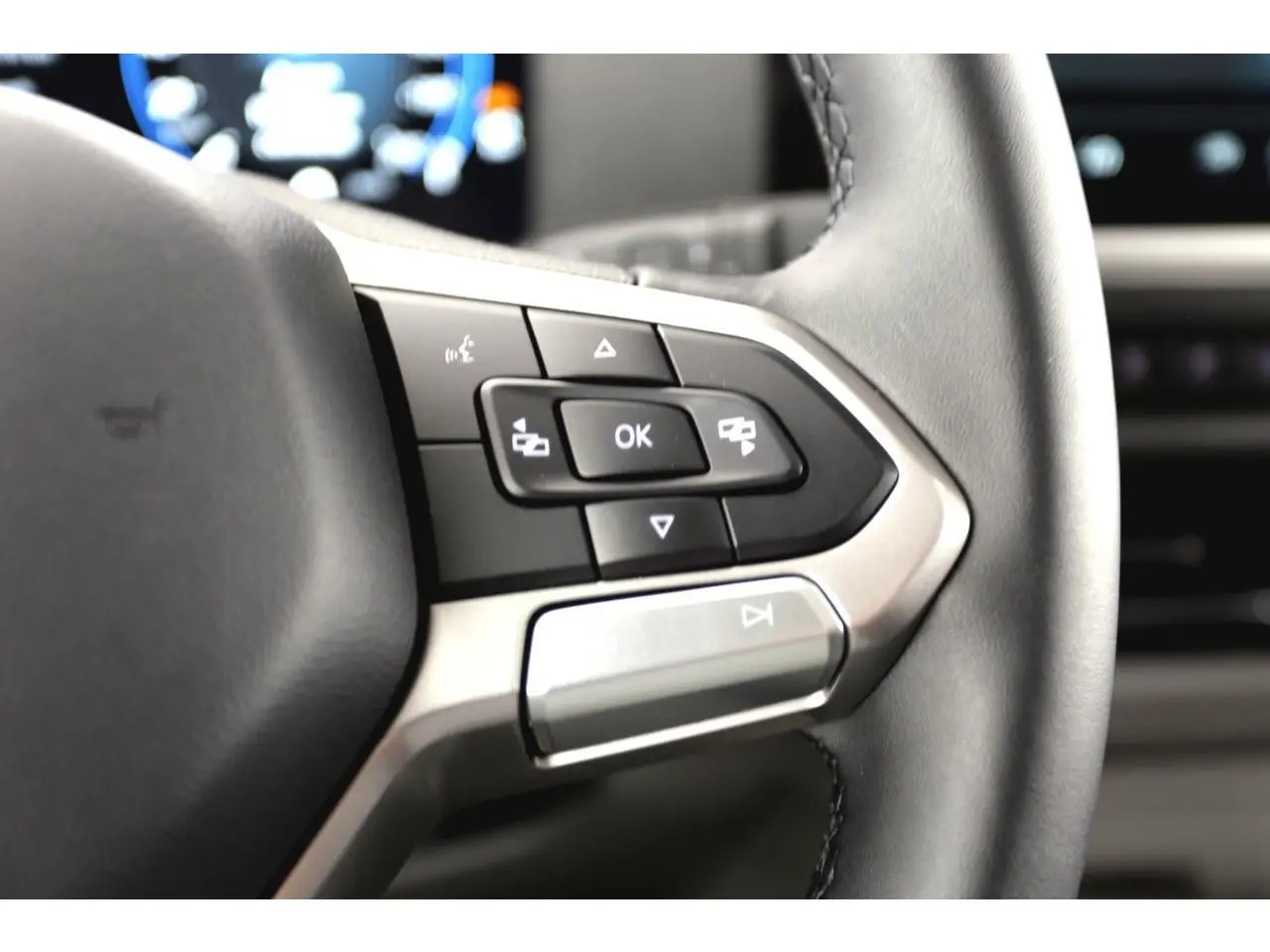 Gros plan sur les commandes multifonctions du volant en similicuir du Volkswagen Transporter gris Stone 2025.