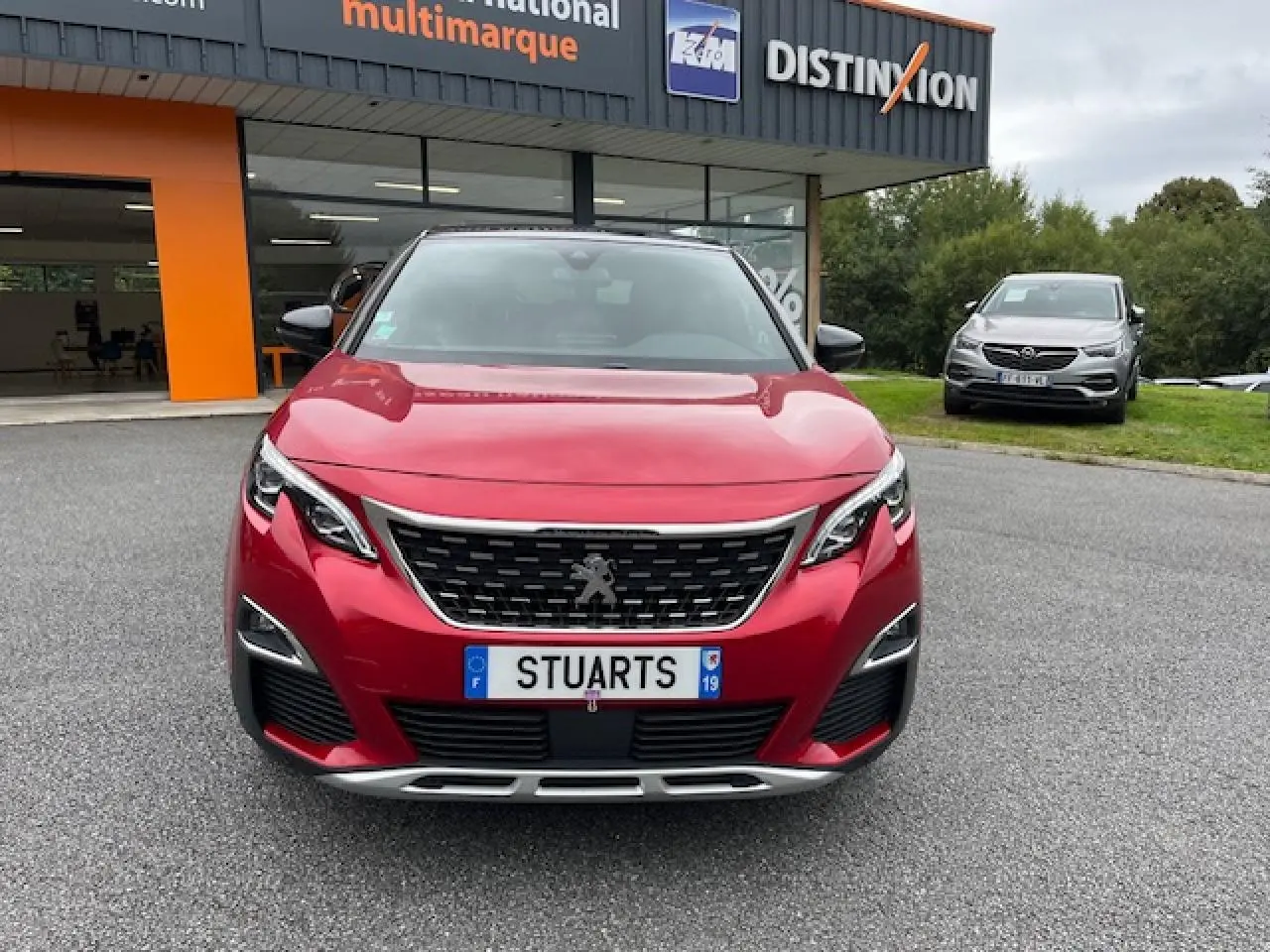 Vue frontale d'un Peugeot 3008 GT Line rouge Ultimate avec calandre chromée et projecteurs LED, devant un showroom.