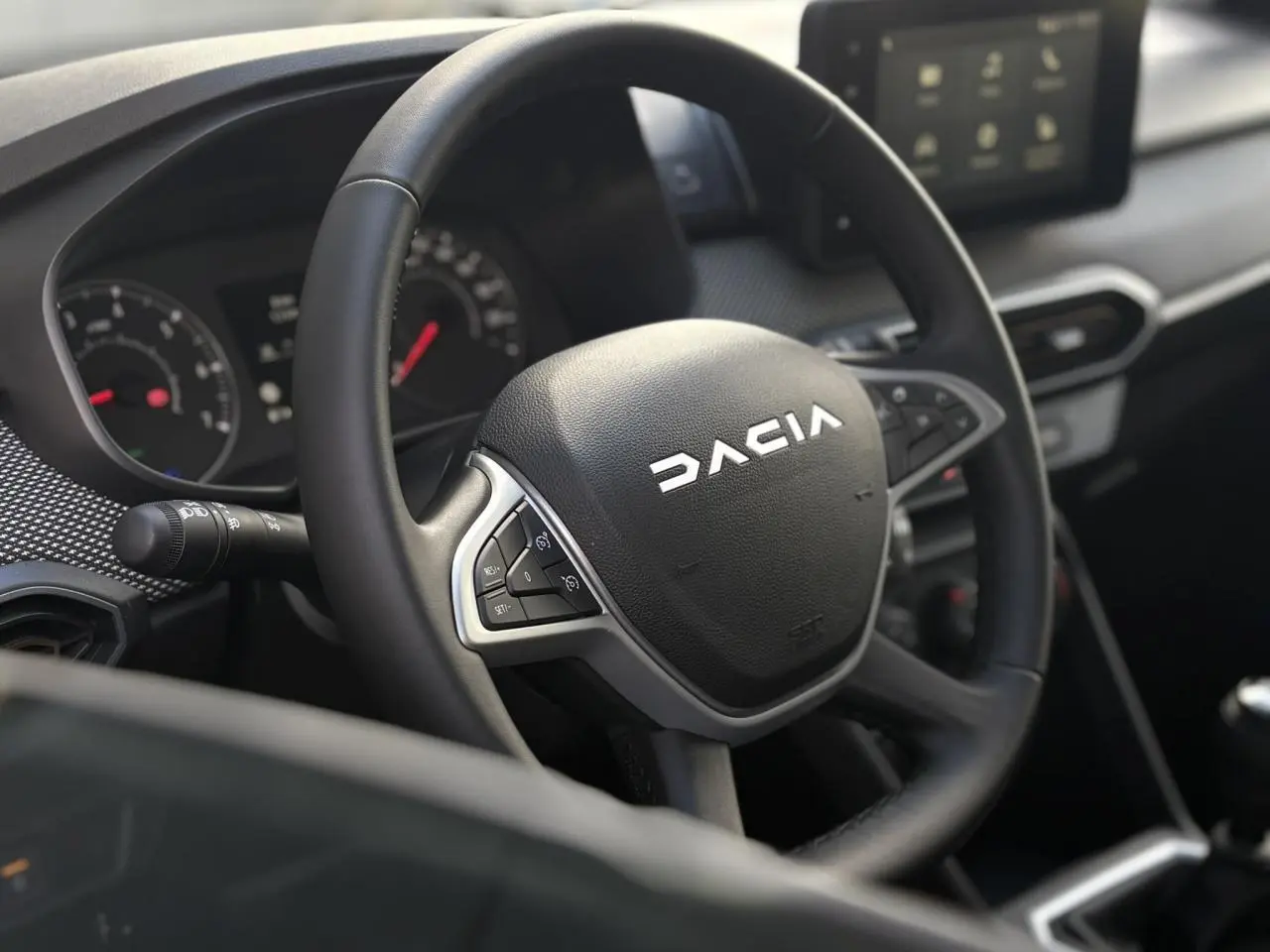 Gros plan sur le volant noir de la Dacia Sandero Stepway 2025 avec tableau de bord et écran tactile en arrière-plan.