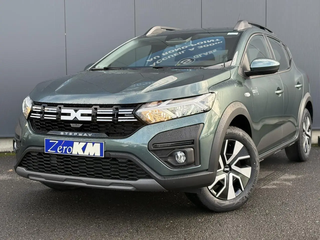 Dacia Sandero Stepway vert cèdre en 3/4 avant droit, avec barres de toit et jantes spécifiques noir et argent.