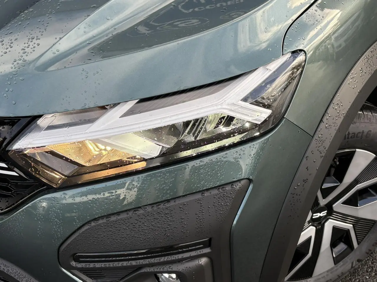 Gros plan sur le phare avant droit et la roue de la Dacia Sandero Stepway 2025 en Vert Cèdre métallisé.