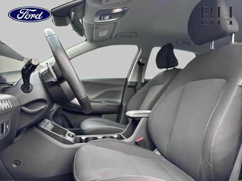 Intérieur avant d'une Hyundai Kona 2023, sièges tissu noir et accoudoir central visible côté droit.