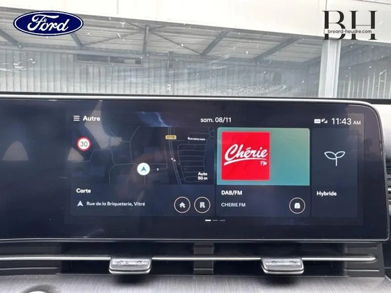 Écran tactile central du Hyundai Kona 2023 affichant GPS, radio Chérie FM et mode hybride dans un intérieur moderne.