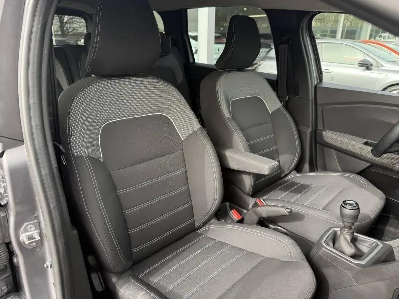 Vue intérieure côté conducteur du Dacia Jogger gris Schiste, montrant les sièges avant en tissu avec surpiqûres blanches et levier de vitesses manuel.