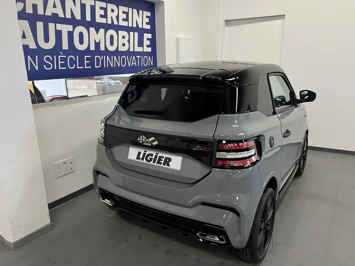Vue 3/4 arrière droite d'une Ligier JS50 grise avec toit noir brillant et feux arrière LED dans un showroom.