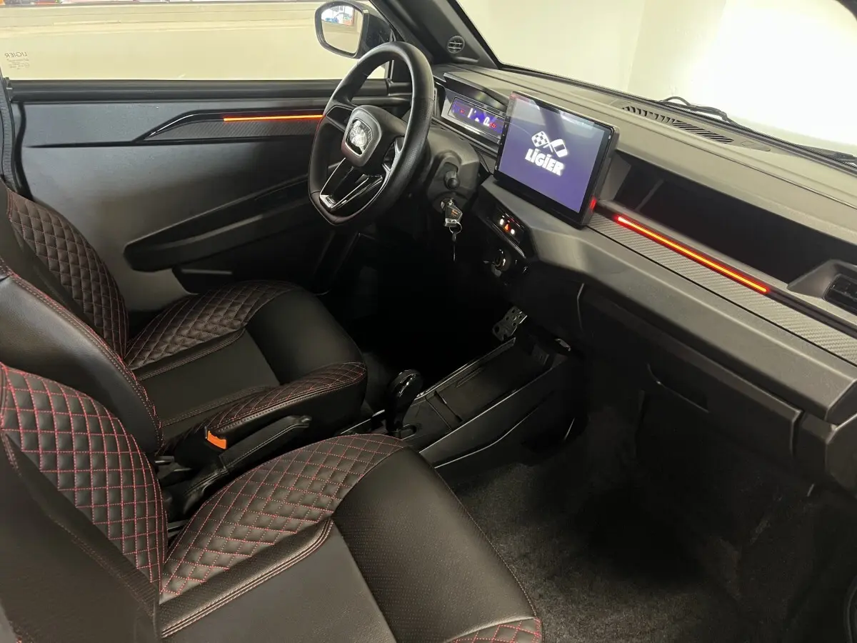 Vue intérieure côté conducteur de la Ligier JS50 bleu, avec sièges noirs à surpiqûres rouges et écran tactile central.