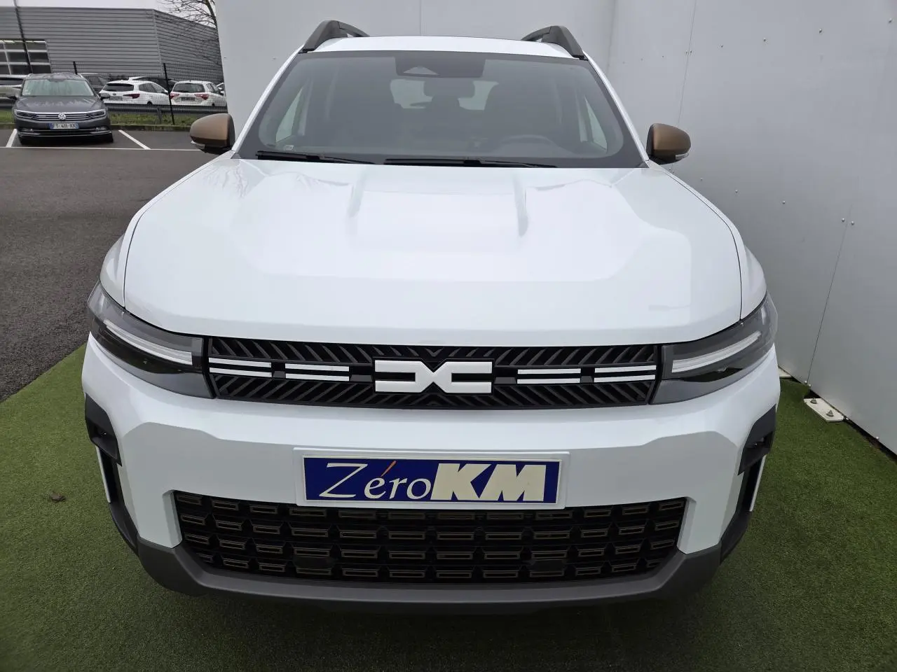 Vue frontale d'un Dacia Bigster blanc glacier avec calandre noire et rétroviseurs brun cuivré visibles.