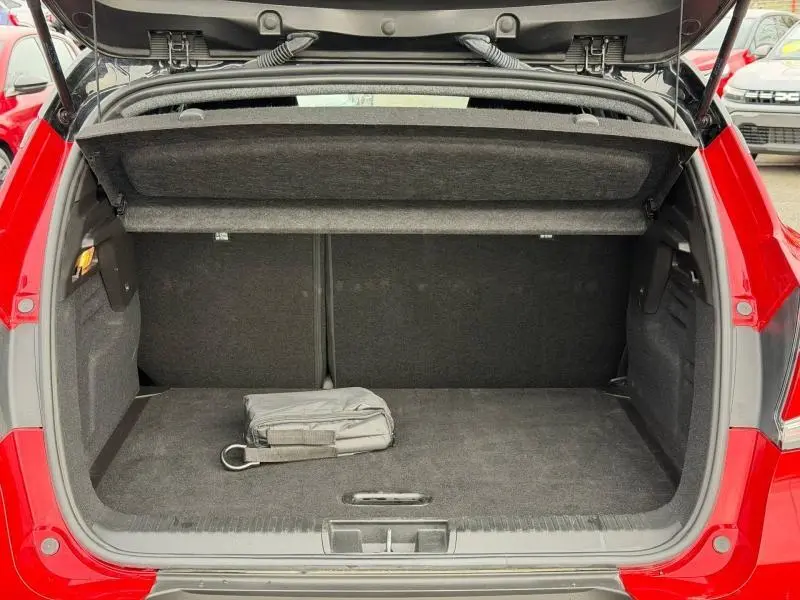 Coffre ouvert vu de l'arrière d'un Renault Captur Rouge Flamme 2025, montrant l'espace de chargement vide avec un sac noir.