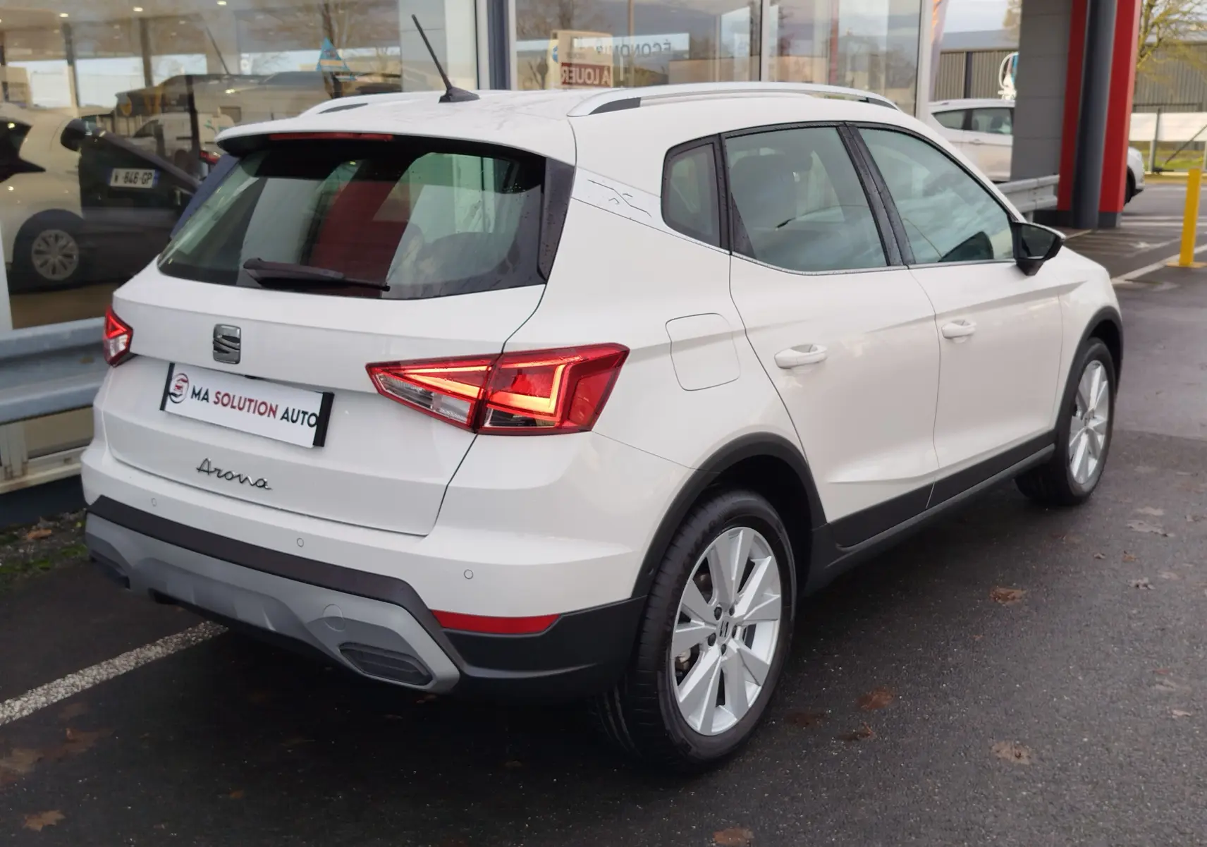 Vue 3/4 arrière droite d'un SEAT Arona blanc Candy 2023 avec feux LED et jantes alliage visibles.
