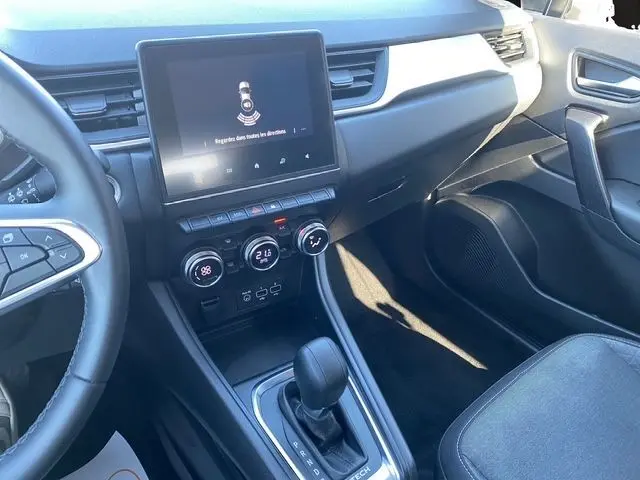 Vue intérieure côté conducteur du tableau de bord et console centrale du Renault Captur gris Cassiopée, avec écran tactile et commandes climatisation.