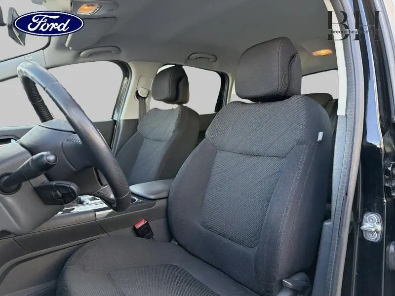 Vue intérieure côté conducteur d'une Peugeot 3008 noire, mettant en valeur les sièges en tissu gris et le volant cuir.