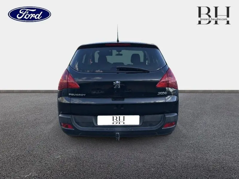 Vue arrière d'un Peugeot 3008 noir Perla Nera avec feux rouges et attelage visible sur un sol gris.