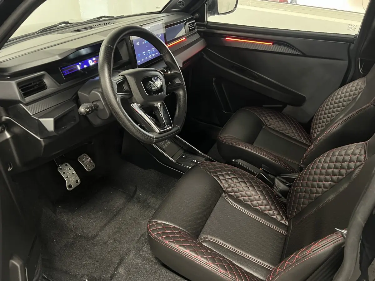 Vue intérieure côté conducteur de la Ligier JS50 Ultimate 2026, sièges noirs avec surpiqûres rouges et tableau de bord digital.