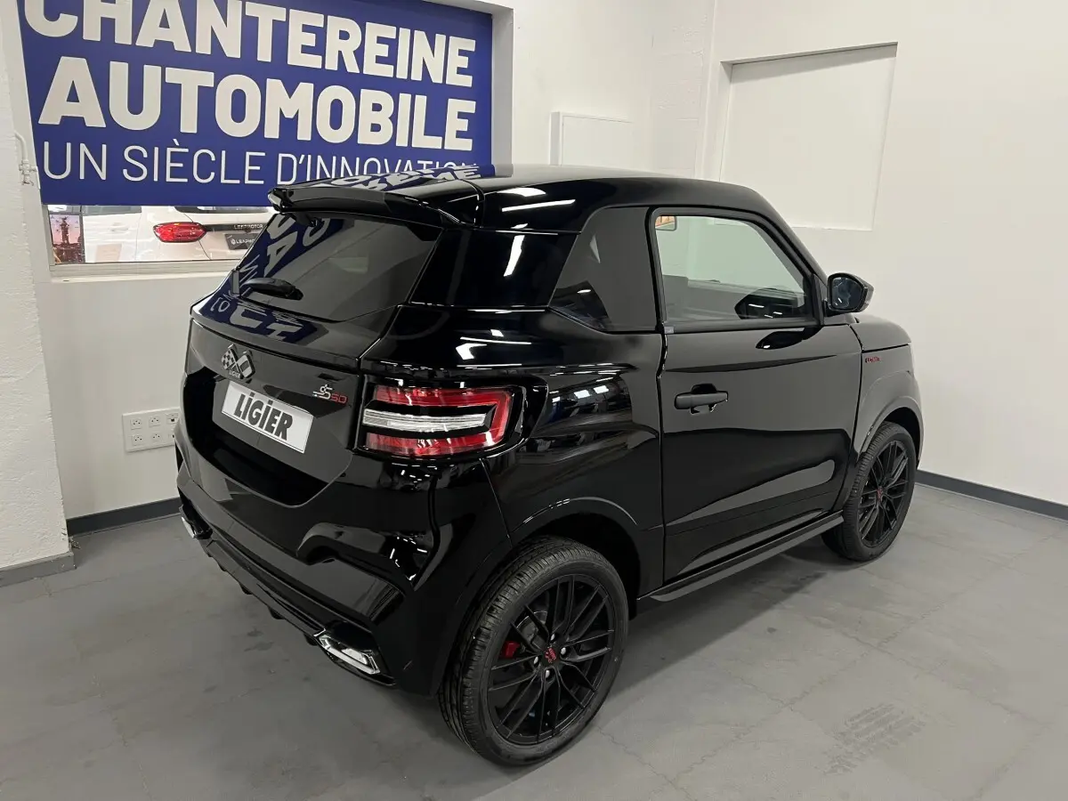 Vue 3/4 arrière droite d'une Ligier JS50 noire mate avec jantes alu noires et feux LED, en intérieur showroom.