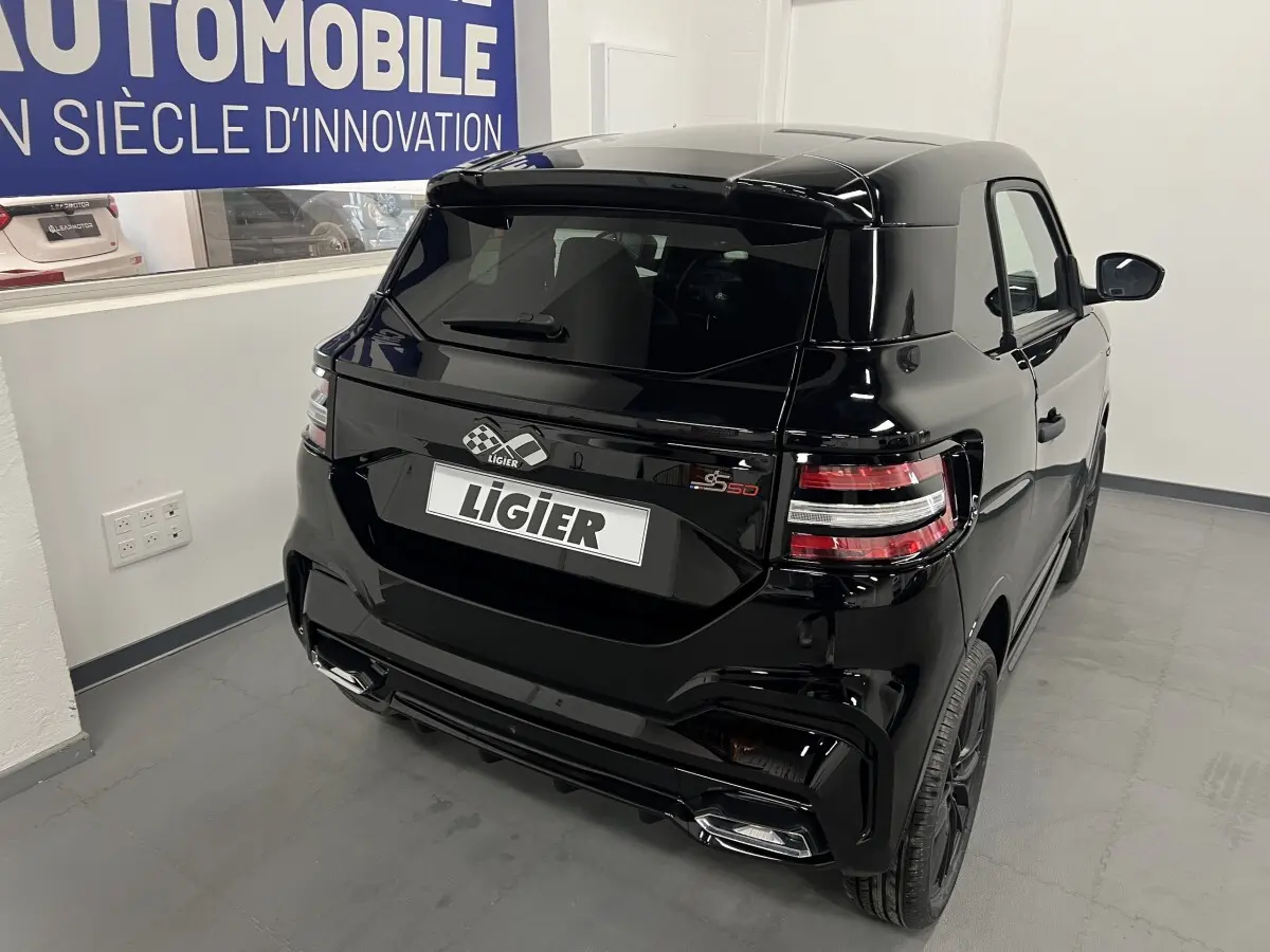 Vue 3/4 arrière droite de la LIGIER JS50 noire avec feux LED et jantes alu noires mates dans un showroom.