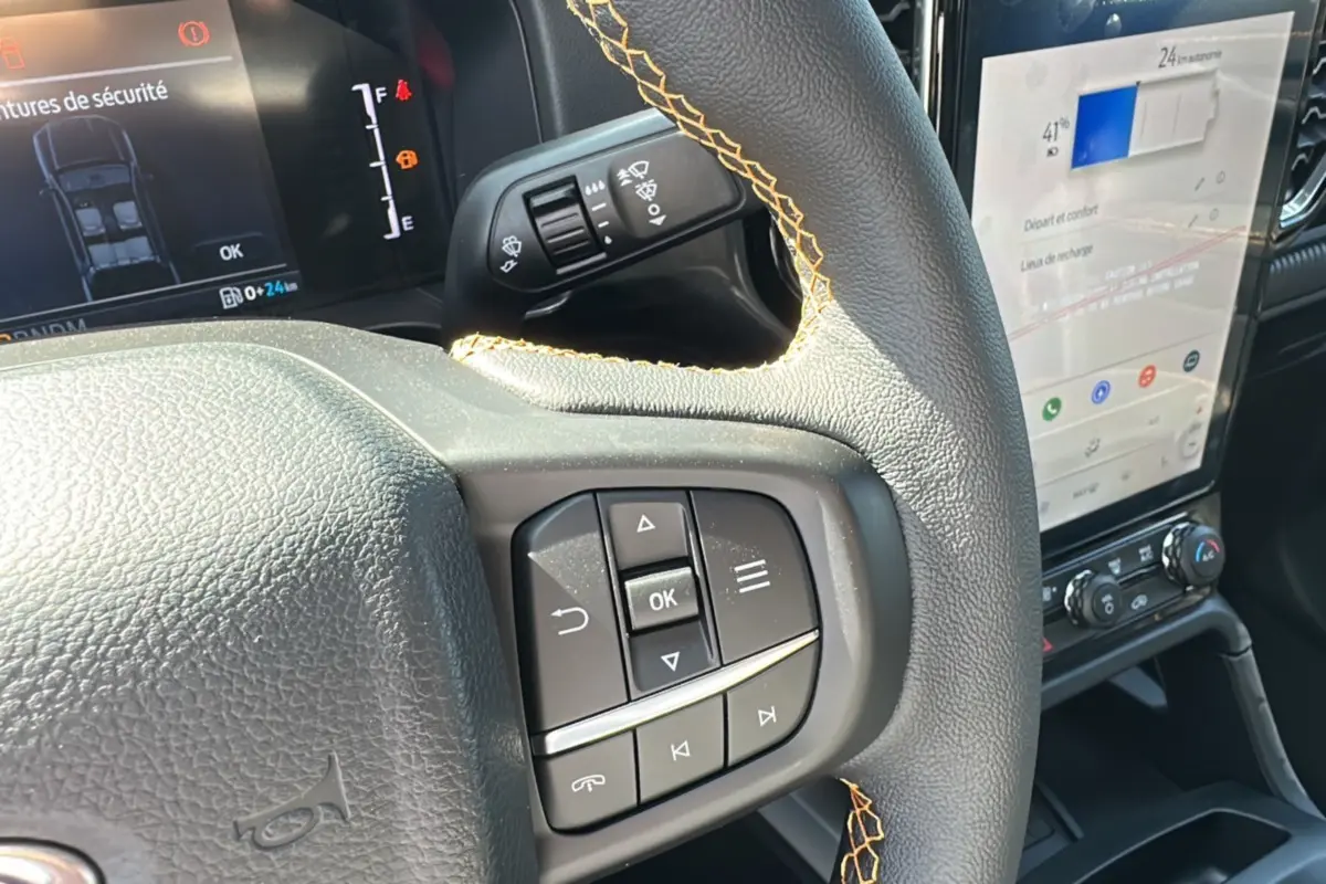 Gros plan sur le volant cuir noir avec surpiqûres jaunes du Ford Ranger blanc, affichage numérique et écran tactile central visibles.