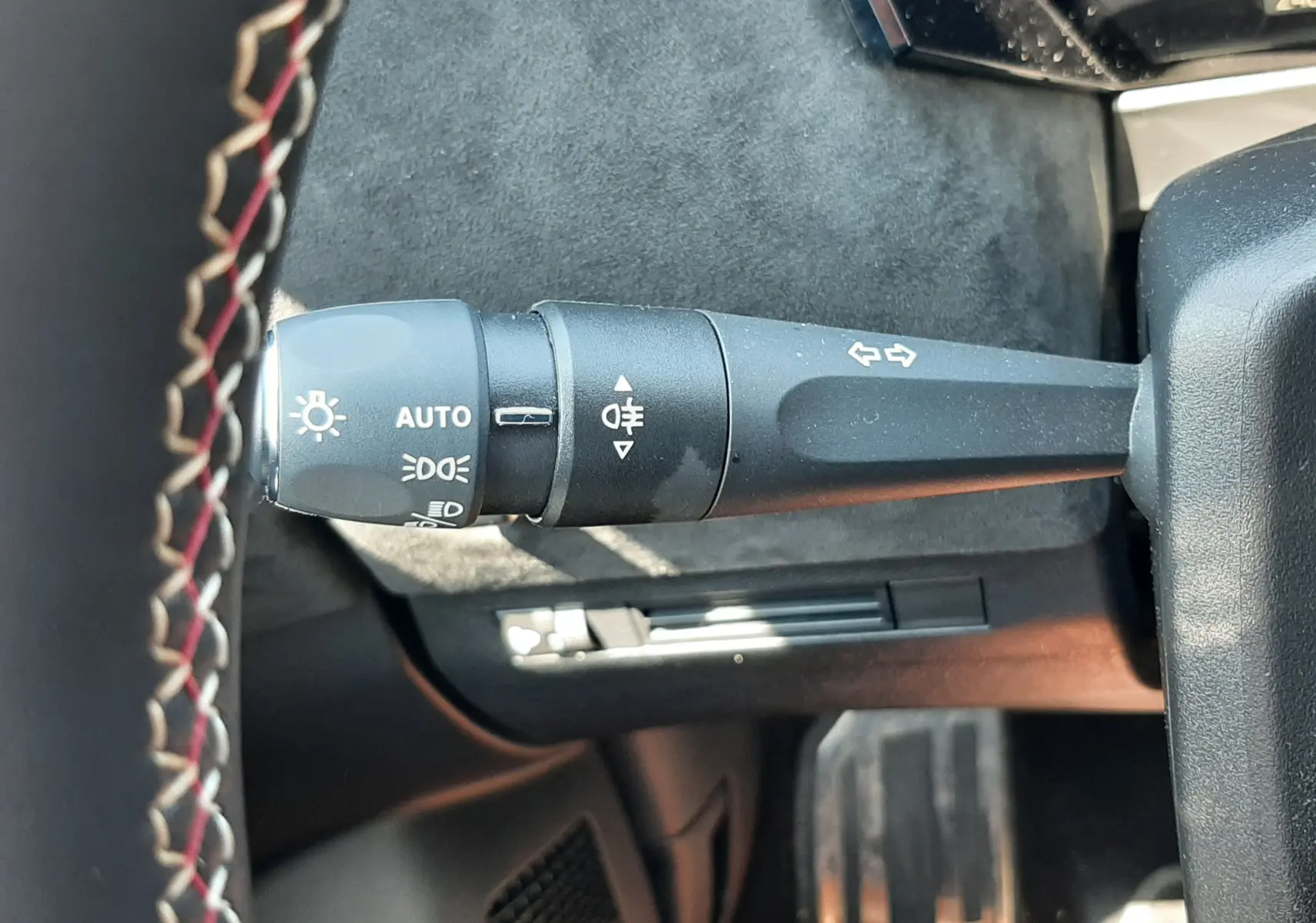 Gros plan sur la manette de clignotants et feux avec marquages blancs, volant cuir noir surpiqûres rouges visible.