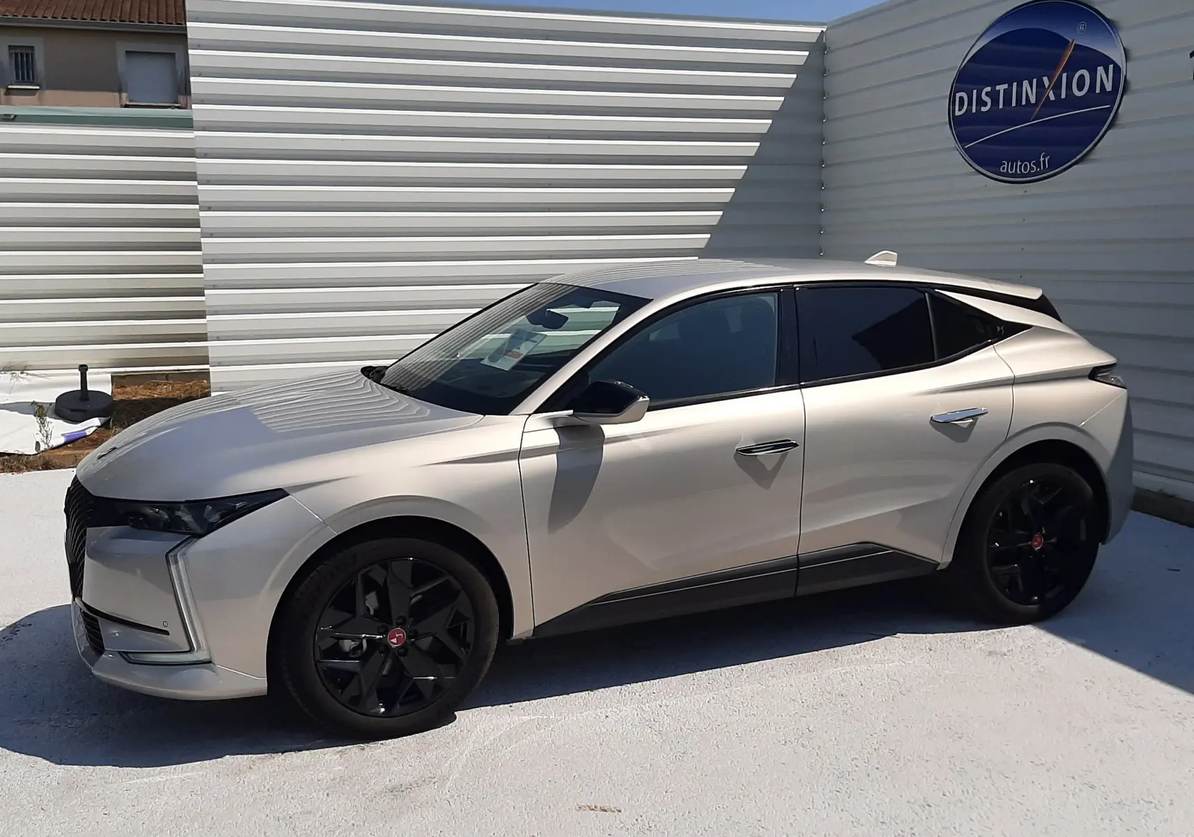 Vue de profil côté gauche d'une DS4 2024 Cristal Pearl avec jantes noires et vitres teintées, stationnée devant un mur blanc.