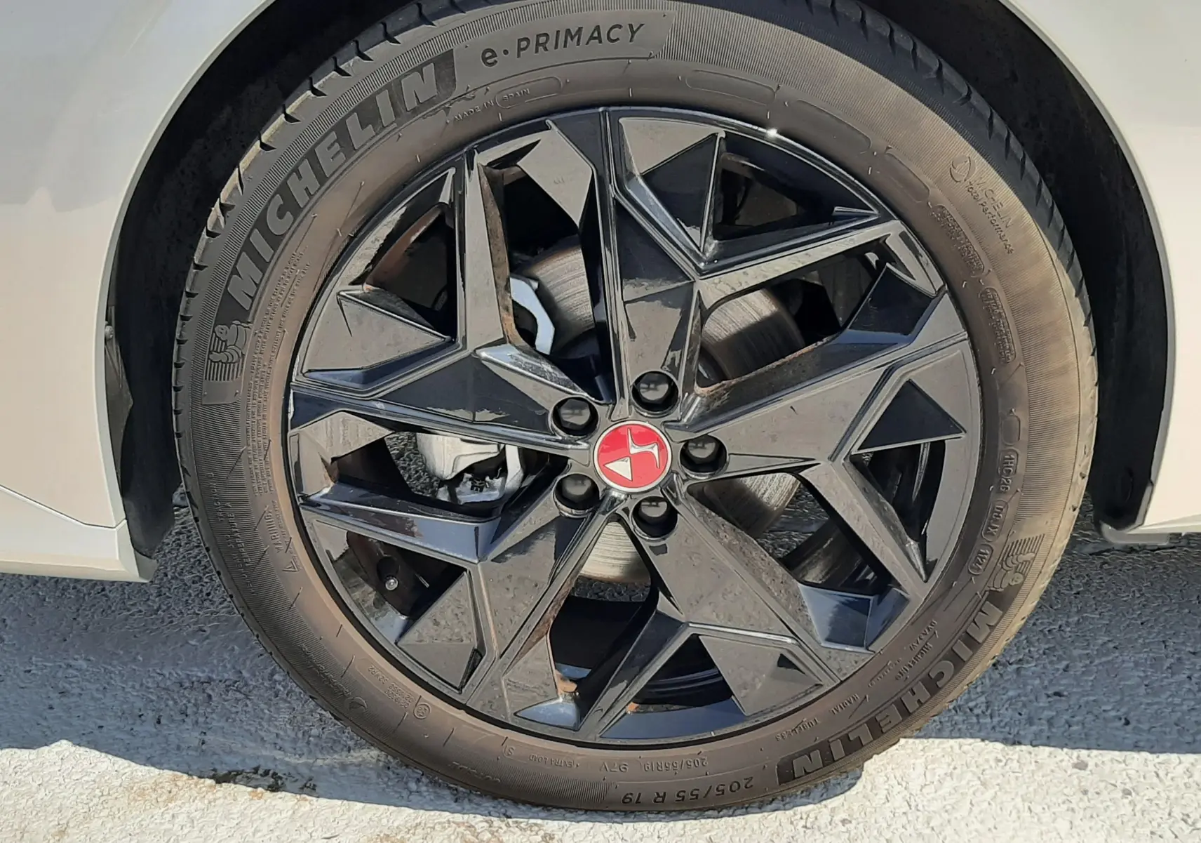 Gros plan sur la roue avant gauche d'une DS4 2024 Cristal Pearl avec jante noire au design géométrique et logo rouge central.