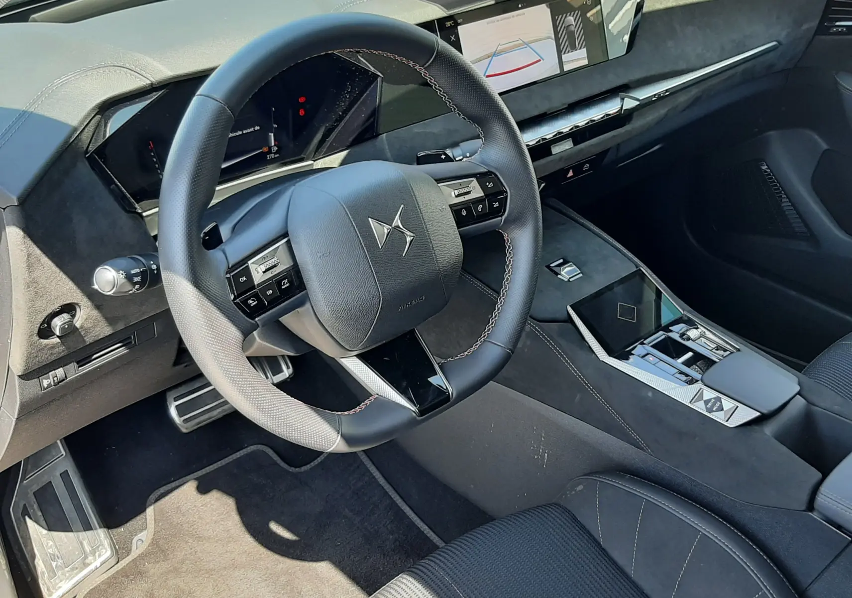 Intérieur noir du DS4 2024, vue du poste de conduite avec volant DS, tableau de bord digital et console centrale moderne.