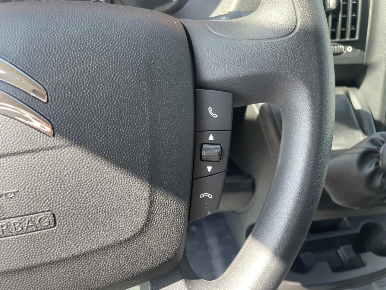 Gros plan sur les commandes Bluetooth du volant noir du Citroën Jumper 2023 avec levier de vitesse manuel visible à droite.