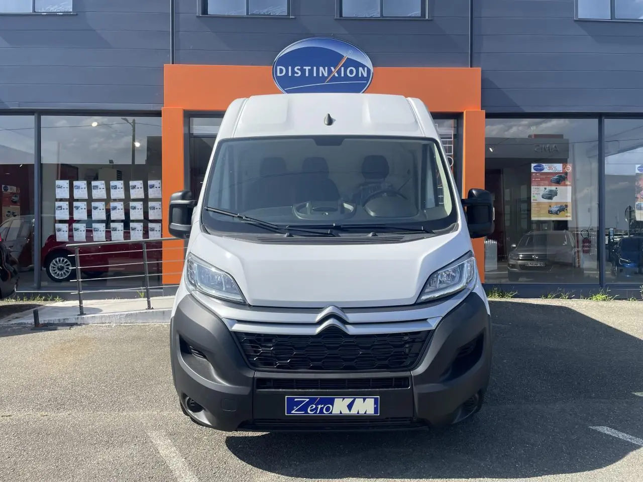 Vue de face d'un utilitaire Citroën Jumper blanc avec calandre noire et plaque Zero KM devant un showroom.
