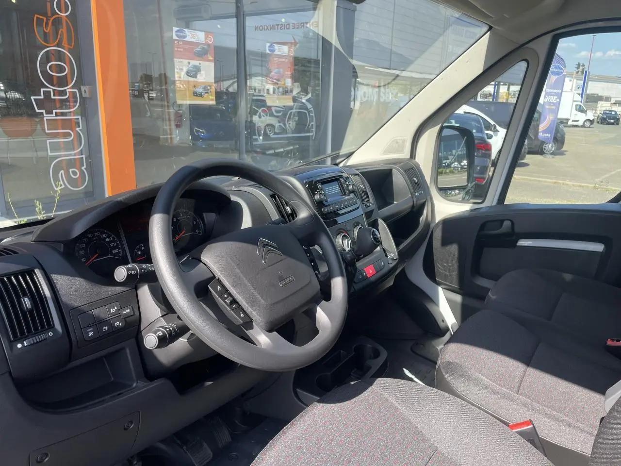 Intérieur du Citroën Jumper 2023 vu côté conducteur, tableau de bord noir avec volant multifonction et banquette passager biplace.