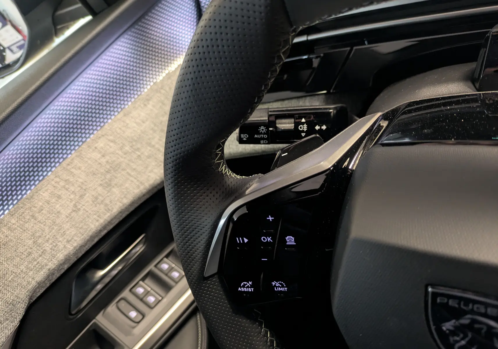 Gros plan sur le volant perforé noir et la portière grise du Peugeot 3008 hybride, avec commandes intégrées visibles.