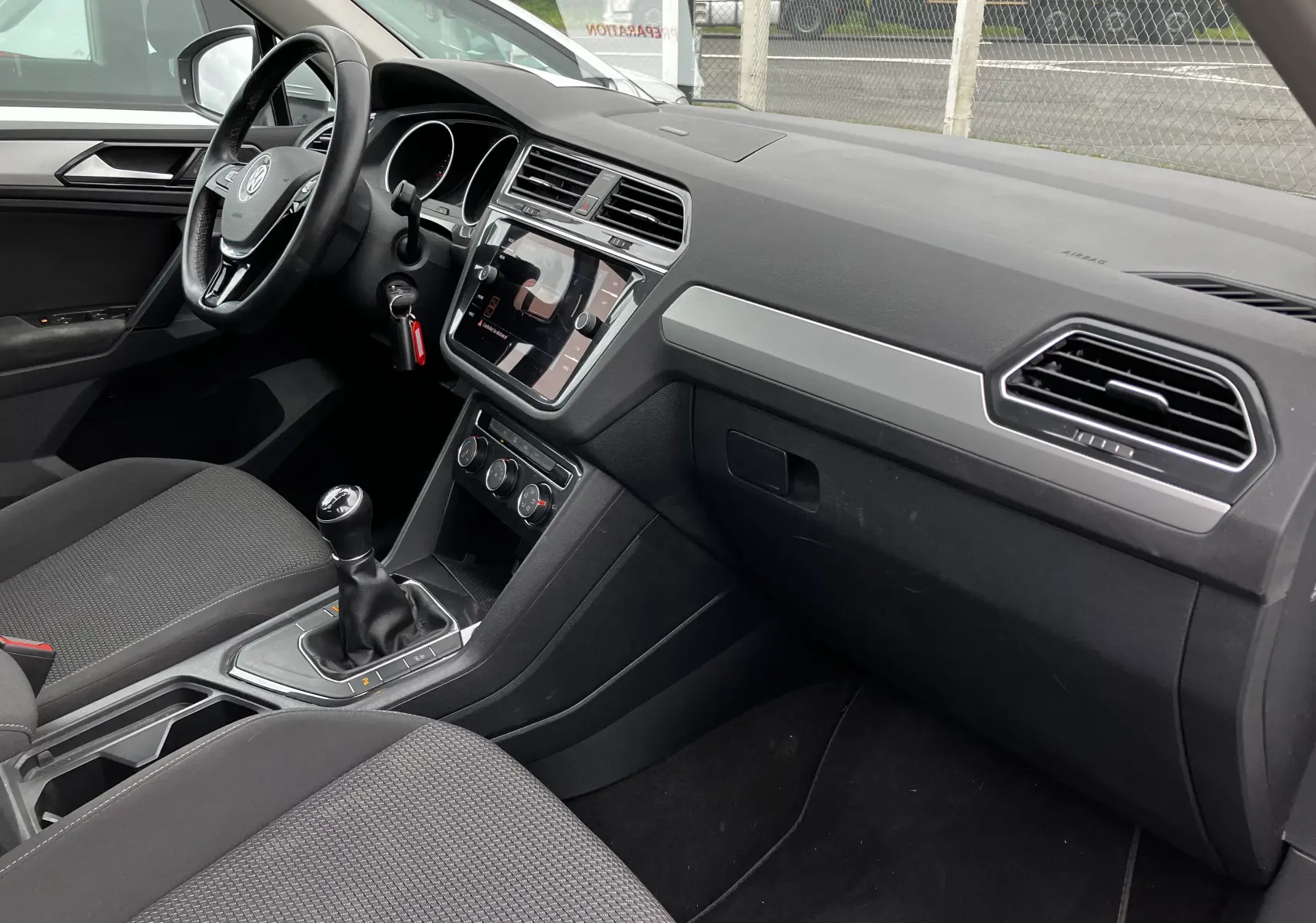 Intérieur côté conducteur du Volkswagen Tiguan blanc 2018, tableau de bord noir avec console centrale tactile et boîte manuelle.
