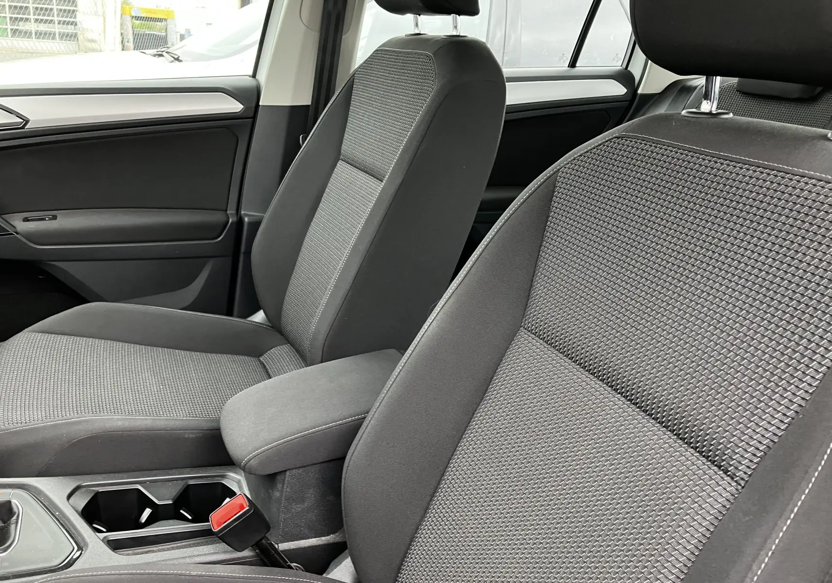 Gros plan sur les sièges avant en tissu gris du Volkswagen Tiguan blanc 2018, avec accoudoir central et ceinture rouge visible.