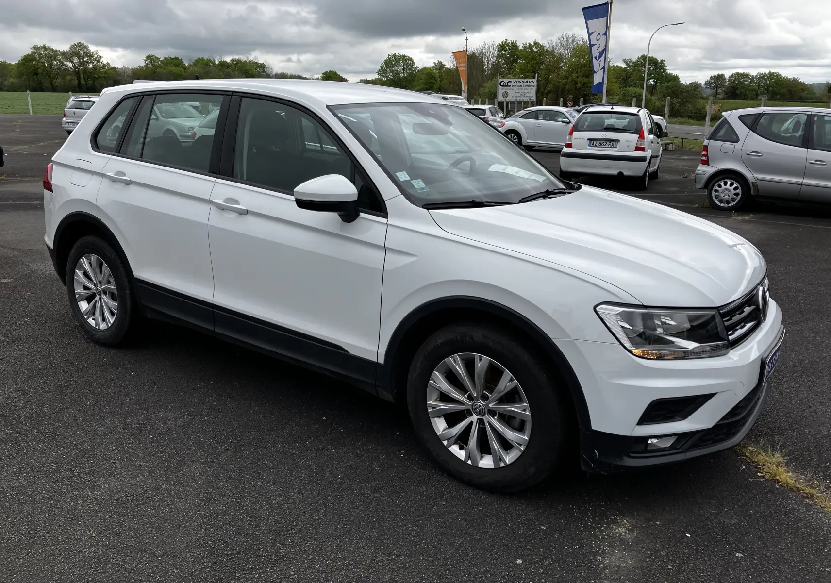 Volkswagen Tiguan blanc vu en 3/4 avant droit sur parking, avec jantes alliage et feux allumés.