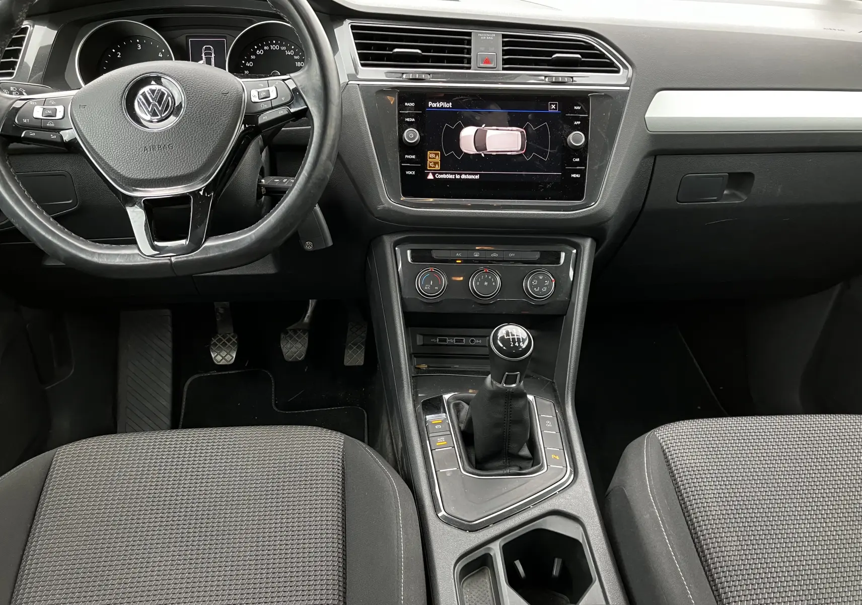 Vue intérieure avant du Volkswagen Tiguan blanc 2018, mettant en valeur le volant multifonction et la boîte manuelle six vitesses.