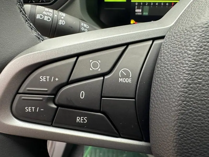 Gros plan sur les commandes de régulateur de vitesse au volant du Dacia Duster blanc 2025, intérieur noir.