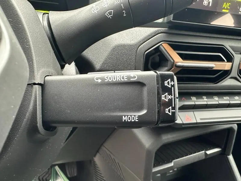 Détail de la commande audio au volant du Dacia Duster 2025, avec tableau de bord gris et aérateurs hexagonaux.