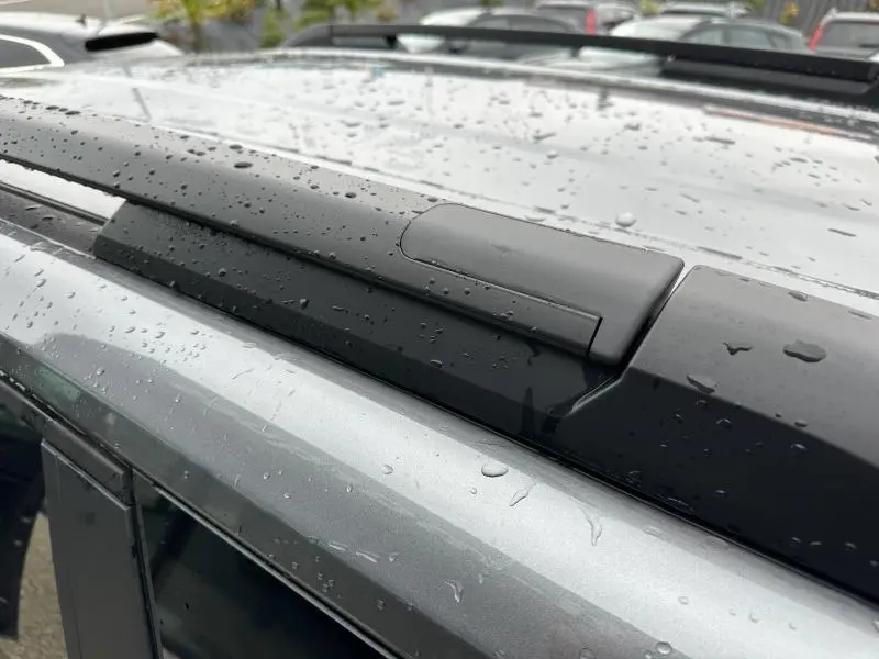 Gros plan sur la barre de toit noire et la peinture gris métallisé d'un Dacia Duster 2025 sous la pluie
