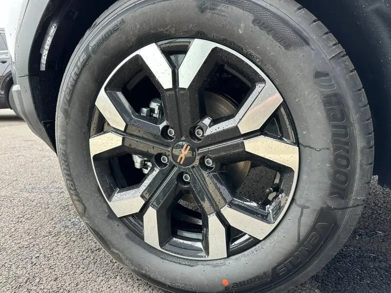 Gros plan sur la jante alliage noire et argentée du Dacia Duster blanc 2025, mettant en valeur le logo central et le pneu Hankook.
