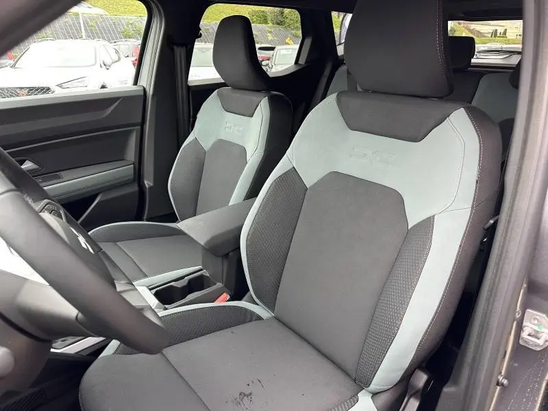 Vue intérieure côté conducteur du Dacia Duster 2025, sièges bi-matière gris clair et foncé avec logo DC brodé.