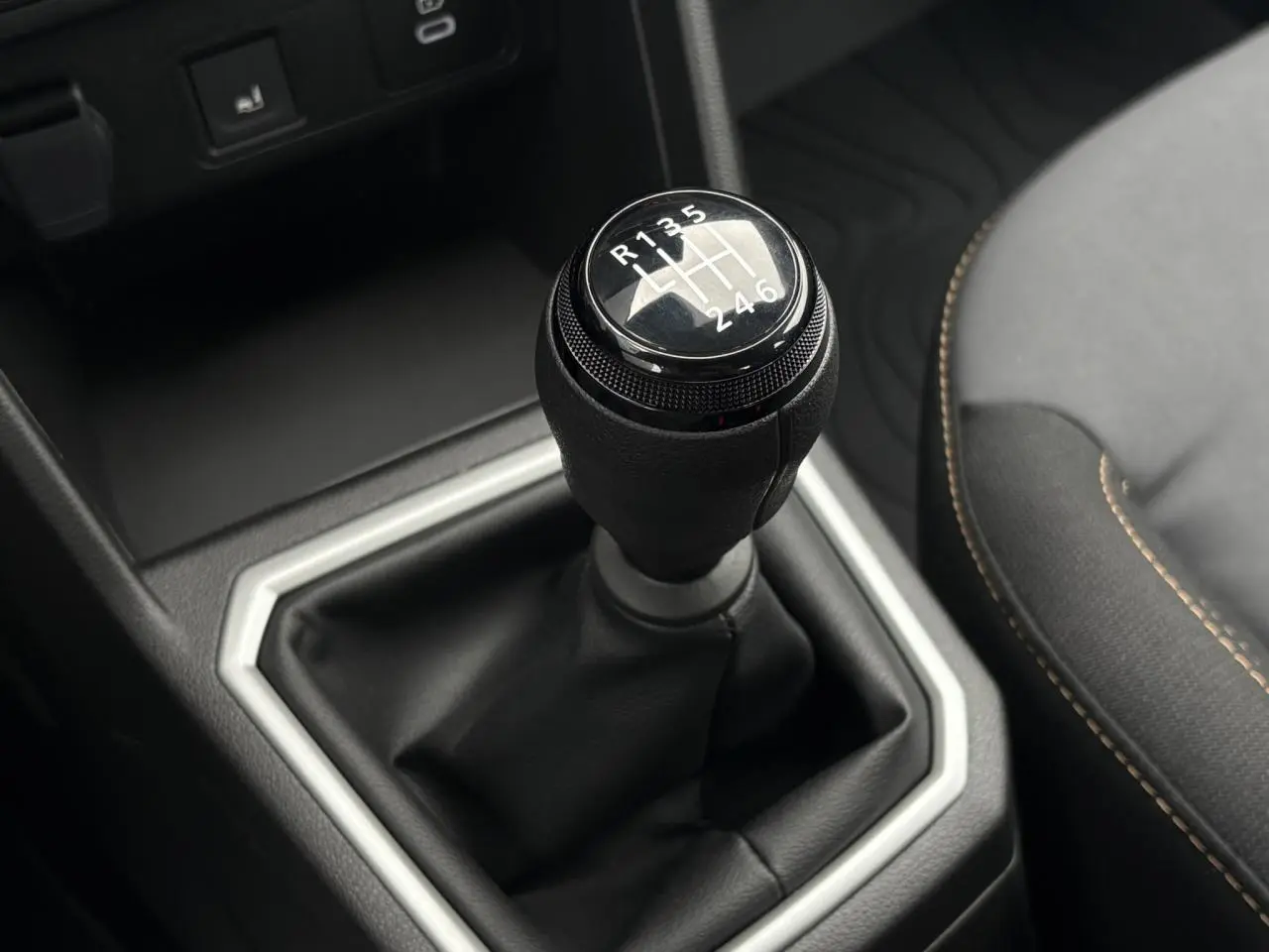 Le levier de vitesses manuel noir de la Dacia Sandero Stepway 2025 vu en gros plan avec sellerie gris foncé et surpiqûres orange.