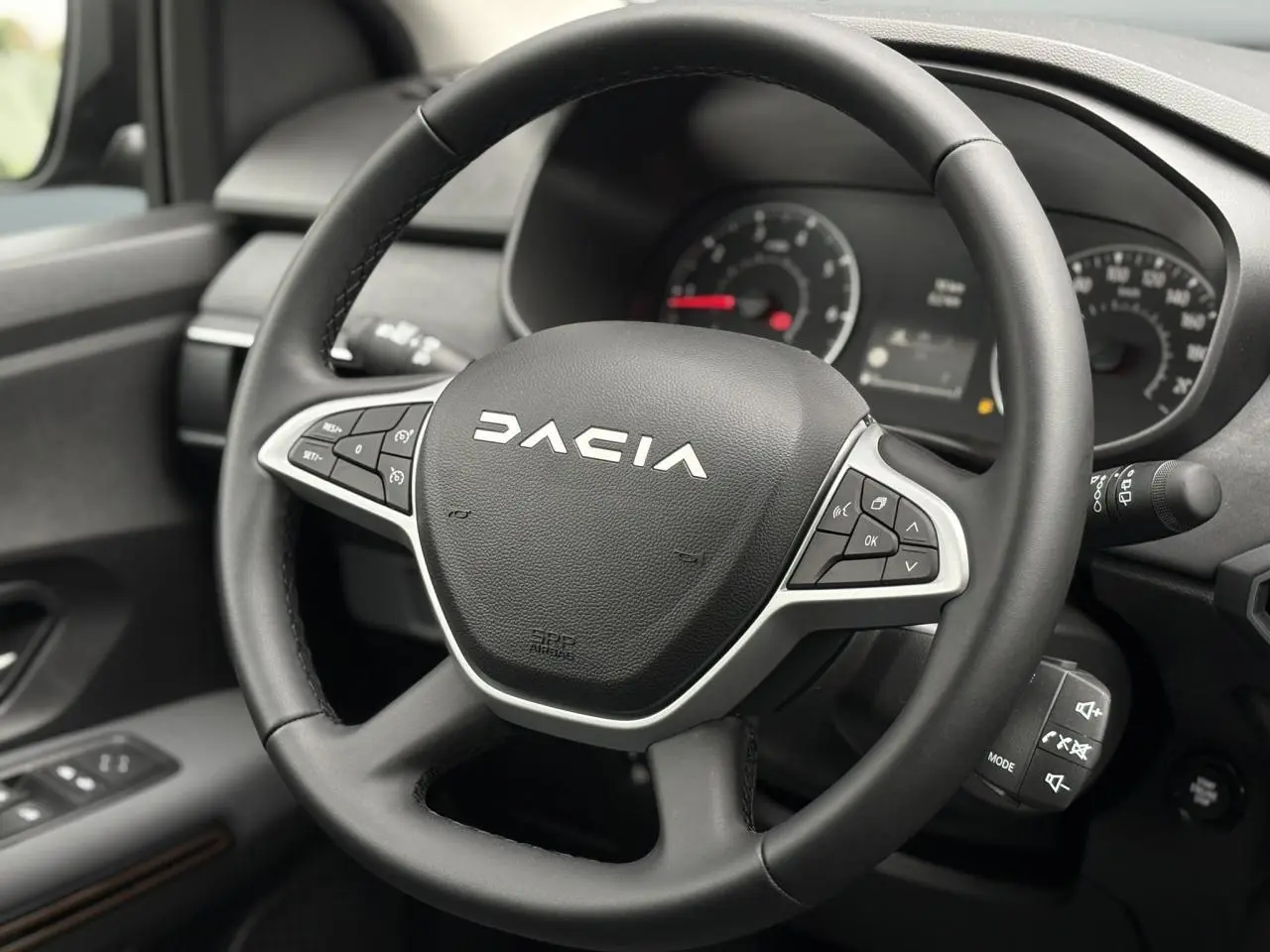 Gros plan sur le volant noir de la Dacia Sandero Stepway 2025, avec commandes intégrées et tableau de bord en arrière-plan.
