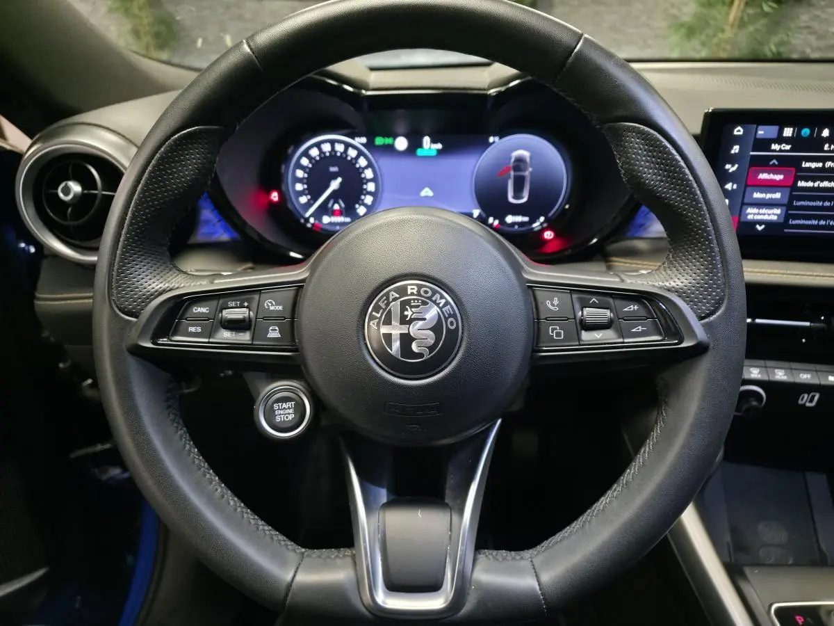 Vue centrée sur le volant sport en cuir noir de l'Alfa Romeo Tonale 2024, avec tableau de bord digital et bouton start/stop visible.