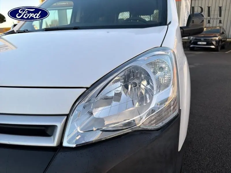 Gros plan sur le phare avant droit d’un Citroën Berlingo blanc, mettant en valeur la calandre et la partie avant du véhicule.