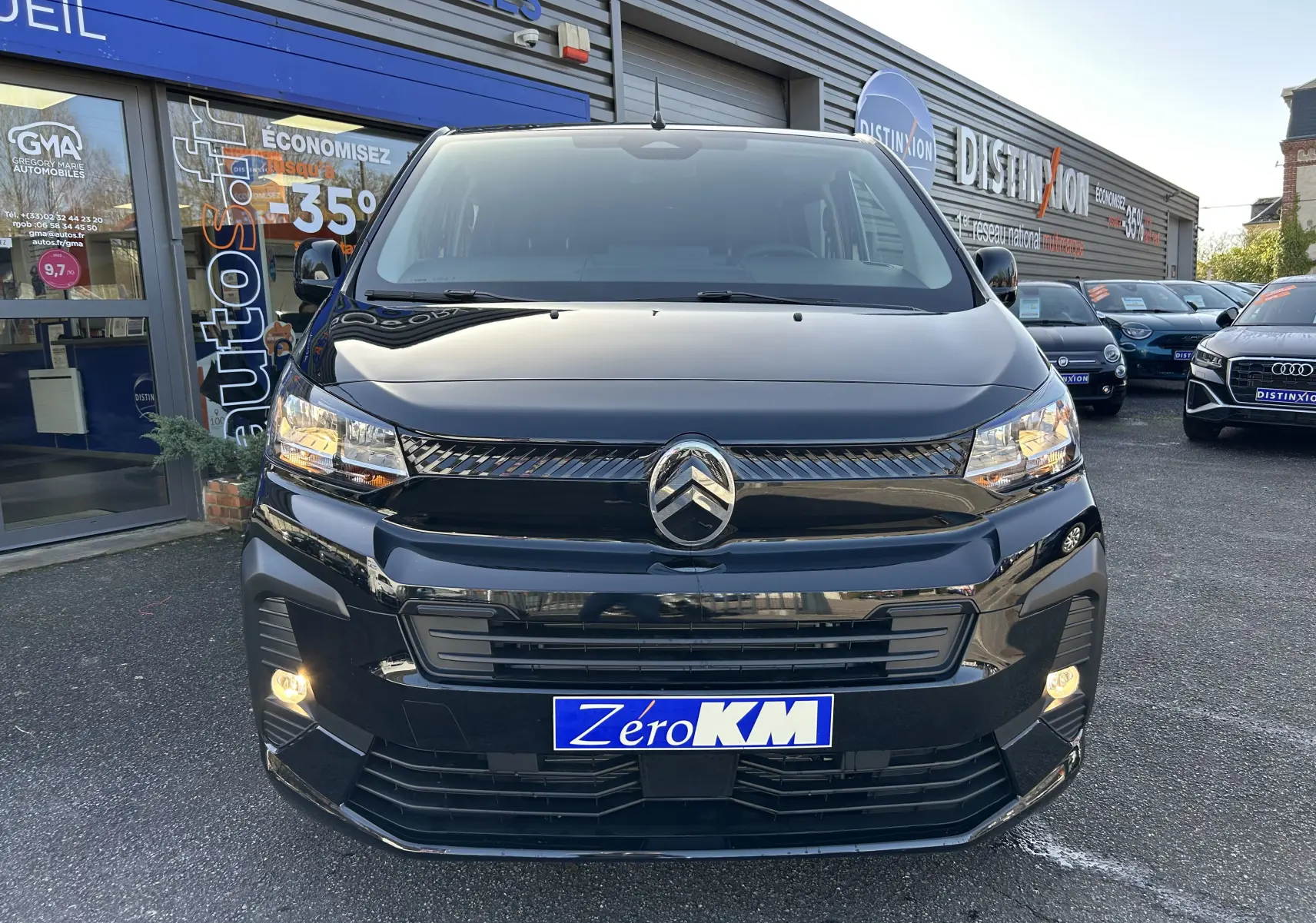 Vue de face d'un Citroën Jumpy Cabine Approfondie noir avec projecteurs allumés sur un parking de concession.