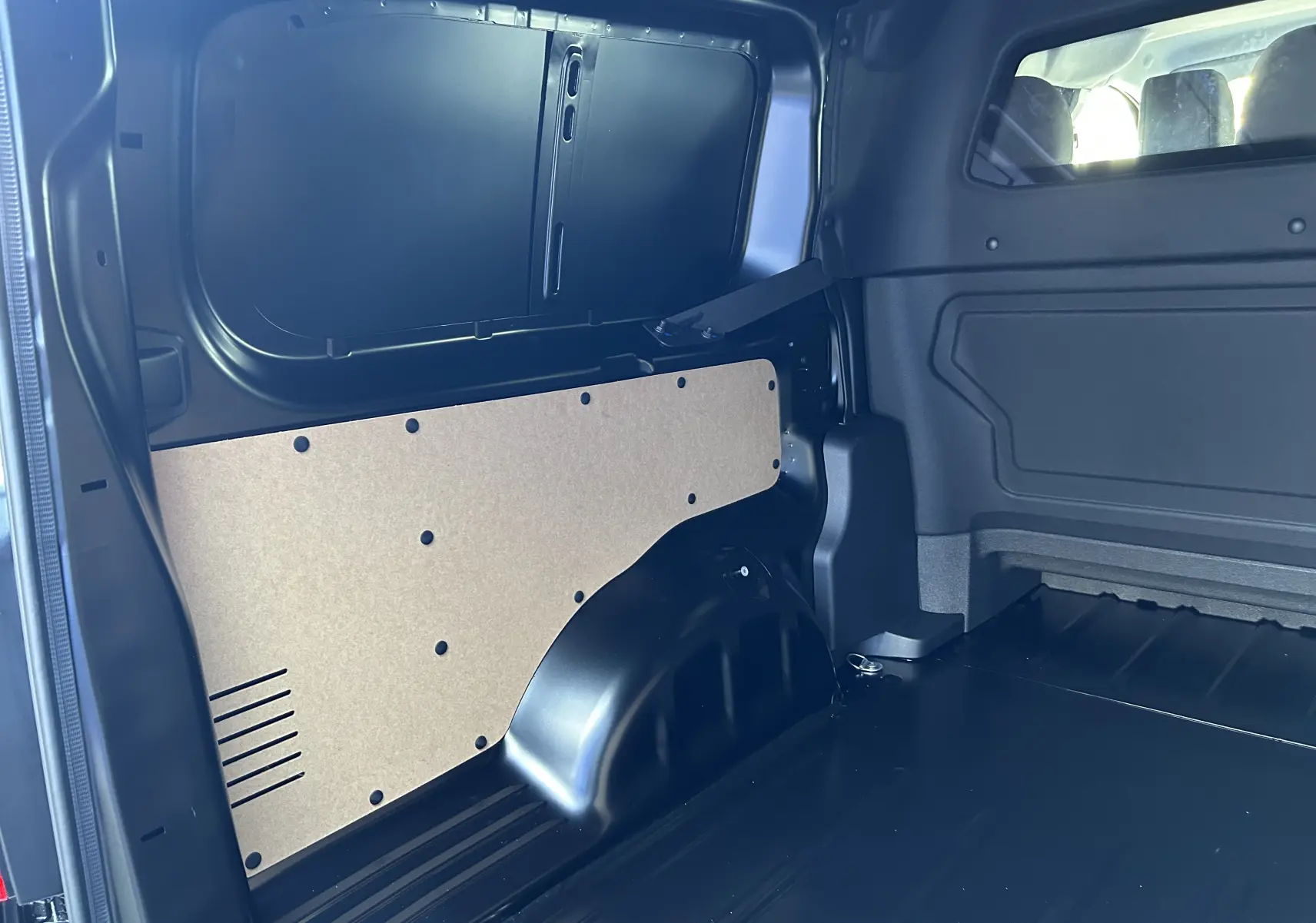 Vue intérieure côté droit de l’espace de chargement noir du Citroën Jumpy Cabine Approfondie 2025 avec panneau de protection beige.