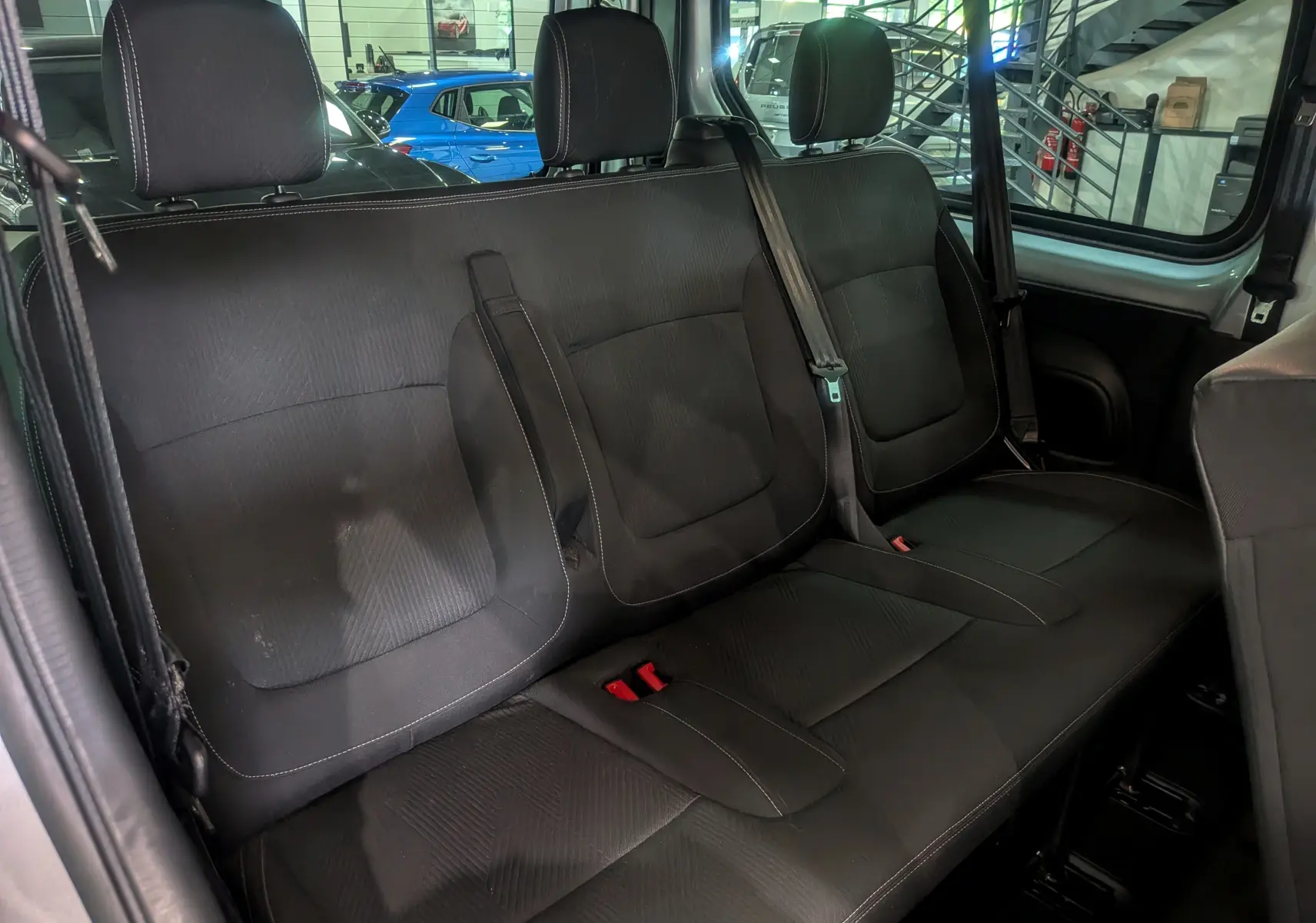 Vue intérieure sur la banquette arrière en tissu noir du Nissan Primastar Combi gris Highland, avec ceintures de sécurité visibles.