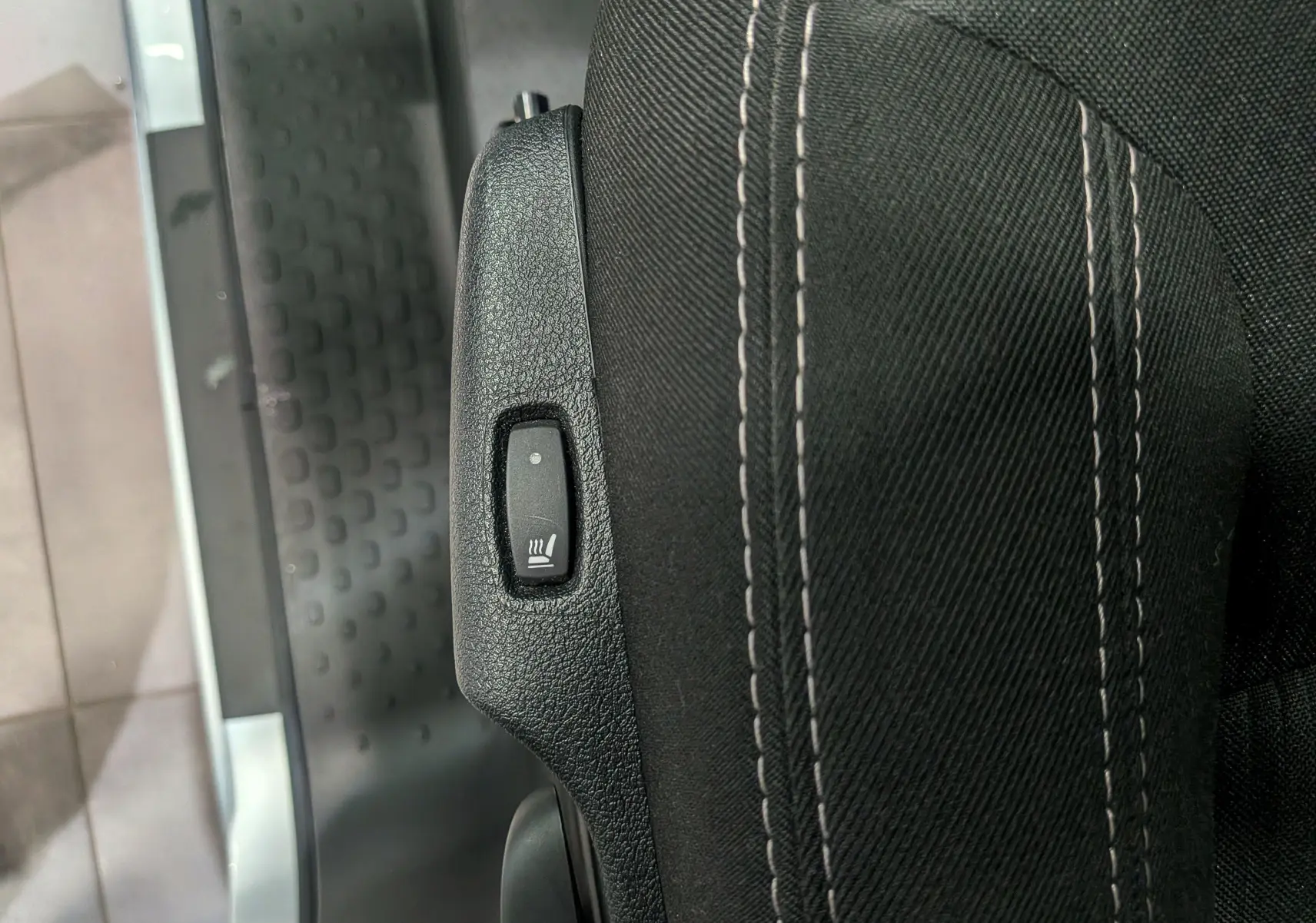 Détail du bouton de chauffage sur le côté du siège en tissu noir du Nissan Primastar Combi gris Highland.