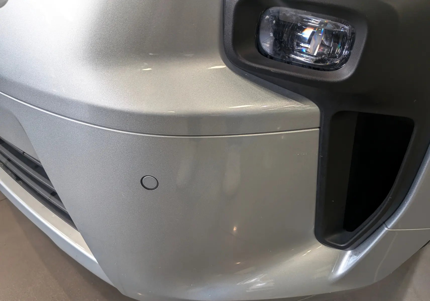 Gros plan sur l'angle avant droit gris Highland du Nissan Primastar Combi, mettant en valeur le feu antibrouillard et le capteur de stationnement.