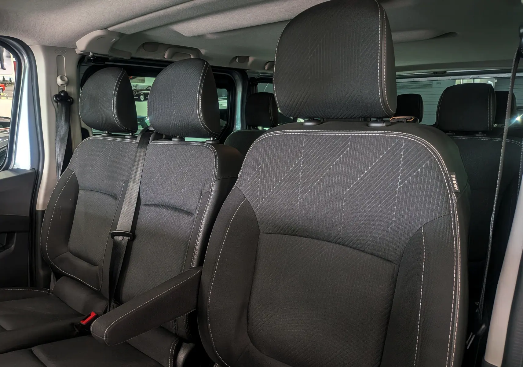 Vue intérieure rapprochée des sièges avant en tissu noir du Nissan Primastar Combi gris Highland, version 2026.