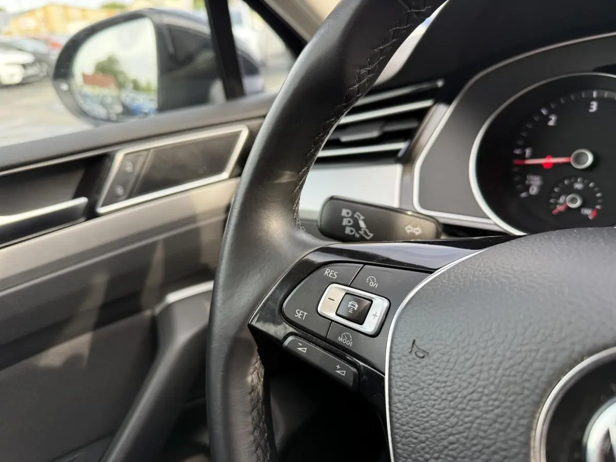 Gros plan sur le volant en cuir noir de la Volkswagen Passat 2018 avec commandes de régulateur de vitesse côté gauche.