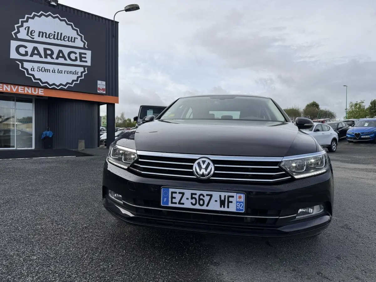 Volkswagen Passat noire vue de face, avec calandre chromée et phares LED allumés sur parking extérieur.
