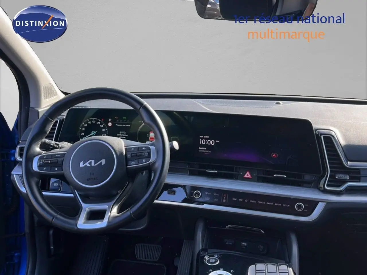 Vue intérieure du tableau de bord et volant du Kia Sportage bleu fusion métal, avec écran digital large et commandes au volant.